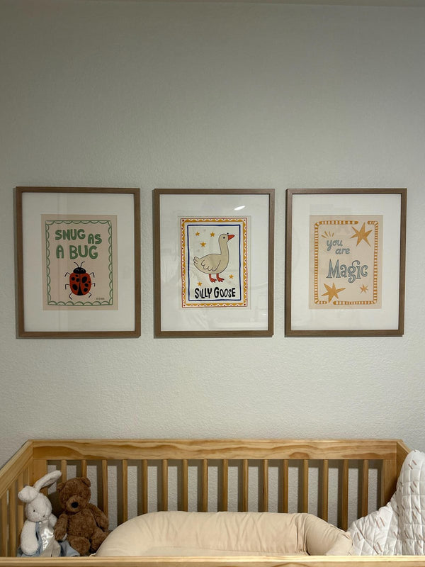 Snug as a Bug, Silly Goose, and You Are Magic prints framed and hung above a nursery crib