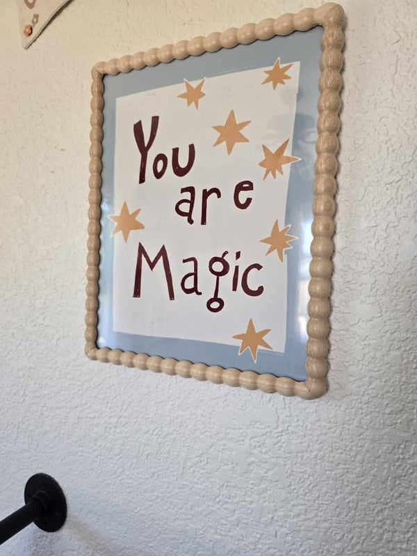 You Are Magic print in a beaded frame hung on a textured nursery wall near a curtain rod
