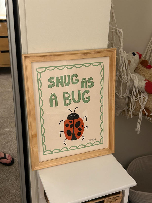 Snug As A Bug ladybug print framed and displayed on a shelf next to a macrame toy hanger in a kids' hallway nook